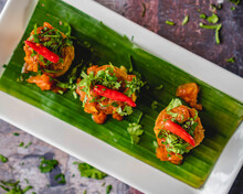 Fish Kebabs With Chili Chutney Served With Red Chili And Coriander On A White Plate With Banana Leaves.