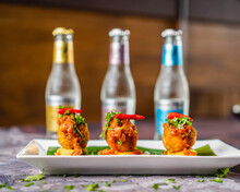 Fish Kebabs With Chili Chutney Served With Red Chili And Coriander On A White Plate With Banana Leaves Bottles In The Background.