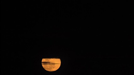 Wall Mural - Timelapse of yellow moon rising in dark night sky, covered and shaded by black clouds