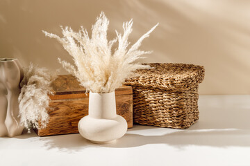 Wall Mural - Beige ceramic vase with pampas grass on the table with wooden box organizer and wicker box at the background, cozy sunlight. Scandinavian home decoration, natural eco materials