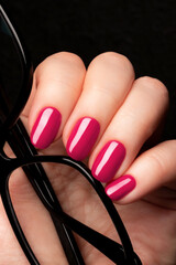 Wall Mural - Female hand with beautiful manicure - viva magenta, pink nails with glasses on black background closeup