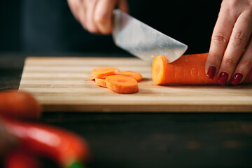 Closeup of female hands slicing carrots on chopping board