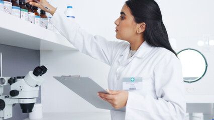 Poster - Medical researcher checking bottles with chemicals inside a modern science lab. Young focused scientist or pharmacist looking at hazardous and dangerous inventory while writing notes in a pharmacy