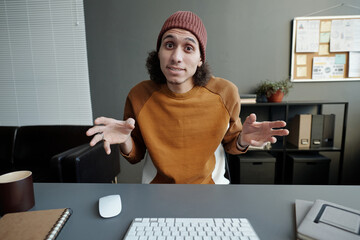 Poster - Young male employee in casualwear sitting by workplace in front of computer monitor and looking at screen during online communication