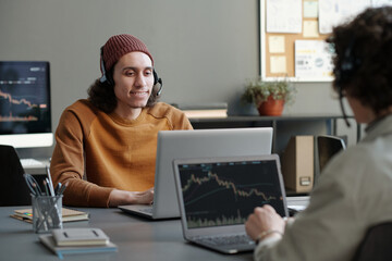 Aufkleber - Young smiling male operator in headset and casualwear consulting online clients while sitting by workplace in office in front of laptop