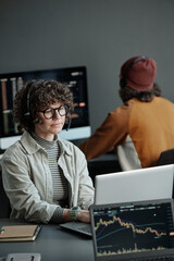 Poster - Young serious female operator of call center sitting by desk in front of laptop, working with online data and consulting clients