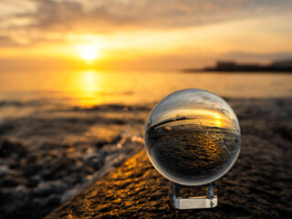 Wall Mural - glass ball on a rough stone by the ocean, sunset sky in the background. warm soft light. selective f