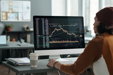 Fototapete - Male analyst sitting in front of computer monitor with graph illustrating development and fluctuations of stock exchange on screen