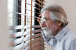 © butsaya33 - Closeup of mature caucasian man looking through window blinds. Curious elderly man peeking through the blinds by the window. Portrait of thoughtful male observing man watching through window blinds.