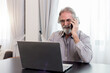 © butsaya33 - Portrait satisfied Caucasian older man talking on the phone with support service center after solved the problem with notebook computer. Smiley happy mature male doing remote online working.