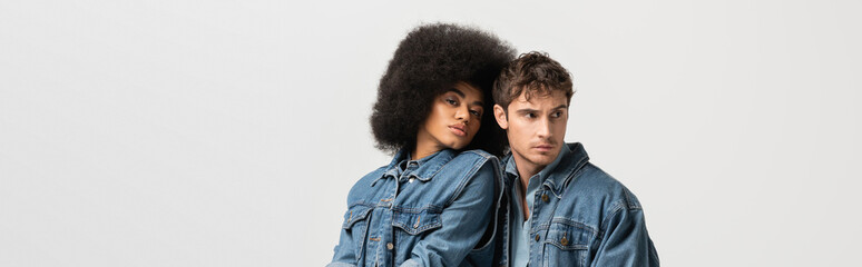 Wall Mural - curly african american woman looking at camera near man in denim clothes isolated on grey, banner.