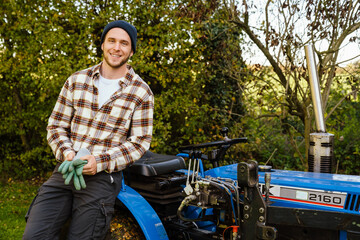 Cheerful man standing near lawn mower while gardening in backyard