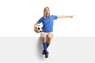 Full length portrait of a female football player sitting on a blank white panel and pointing