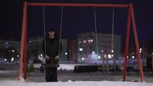 Mentally Ill Depressed Man On Empty Children Playground With Swing On Iron Chains At Winter Night. Concept Of Child Kids Abduction