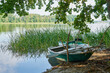 Rowing boats moored on the shore of a lake surrounded by forest during a sunny morning.