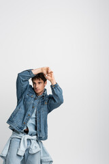 Wall Mural - stylish young man in denim jacket and jeans posing with hands above head isolated on grey.