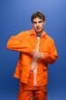 Trendy man posing in orange overall and jacket isolated on blue.