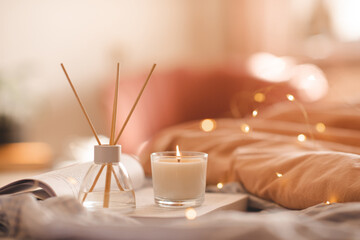 Wall Mural - Liquid home perfume in glass bottle and bamboo sticks with scented candle stay on paper book in bed over living room close up. Cozy atmosphere. Aromatherapy.