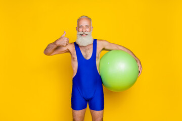 Poster - Portrait photo of old age grandfather handsome gray hair bearded showing thumb up like recommend hold fitness ball isolated on yellow color background