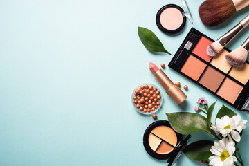 Fototapete - Cosmetic products on blue background. Cream, powder, shadow, brushes with green leaves and flowers. Flat lay image with copy space.