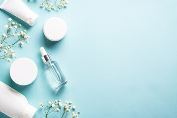 Poster - Natural cosmetic products at blue background. Cream, serum, tonic with green leaves and flowers. Flat lay image with copy space.