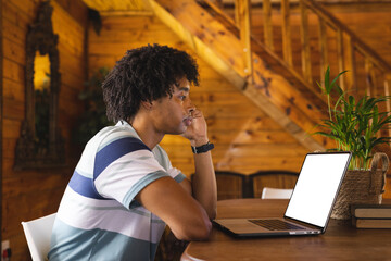 Wall Mural - African american man spending time in log cabin and having laptop video call with copy space