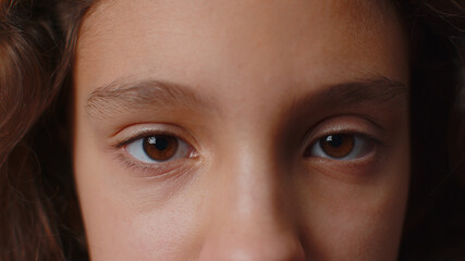 Extreme close-up macro portrait of smiling girl face. Teen beautiful kid's eyes, looking at camera. Brown eyes of brunette female child model. Young positive cute children opening wide her closed eyes