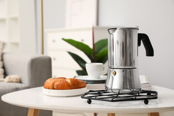 Grid with geyser coffee maker, cup of espresso and delicious croissant on table in living room