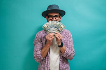 Wall Mural - Excited happy young male winner feeling joy while holding money won, winning lottery, placing bets, getting cashback online gift on blue background. Human face emotions and betting concept.