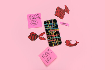 Sticker - Mobile phone with rubber bands and paper decor on pink background. April Fool's Day celebration