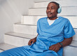 © Courtney/peopleimages.com - Break, music and African doctor with headphones for a podcast, radio and audio on hospital stairs. Freedom, thinking and a male nurse listening to a track or songs while working in healthcare