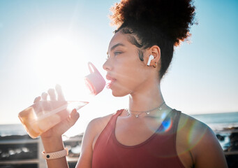 Drinking water, fitness and black woman on beach exercise, listening to music and cardio training in blue sky lens flare. Liquid bottle for diet, goals and tired sports runner or USA person by ocean