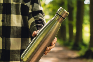 Wall Mural - Close-up of Unrecognizable female hand holding Water bottle. Reusable steel thermo water bottle in park. Sustainable lifestyle. Plastic free zero waste free living. Go green Woman 