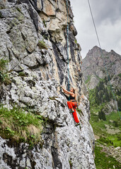 Wall Mural - Woman athlete climbing on the high rock in the mountains