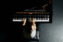 A Woman With Brown Hair Dressed In A White Dress Seen Playing A Black Grand Piano With The Lid Raised. View From Above Of The Pianist To Her Body And Half Of The Piano