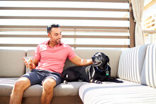 A Man Relaxes Outdoors With A Drink And His Dog.