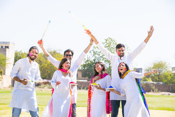 Group of happy young Indian people celebrating holi festival at park outdoor, Playful adult male and friends with colorful paint faces playing with gulal.