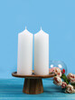 Two white candles on a dark marble table with a bouquet of flowers