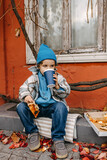 Fototapeta Sport - Little boy eating pizza and drinking soda, outdoors, sitting on city street.