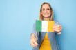 © Danko - Young woman holding Irish flag isolated on blue background.