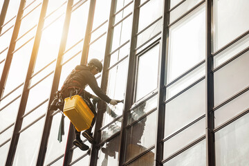 industrial mountaineering worker hangs on facade skyscraper building, washing exterior facade glazin