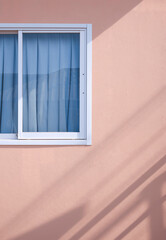 Sunlight and shadow on surface of Glass sliding window with blue curtain on pink gypsum board wall in vertical frame  