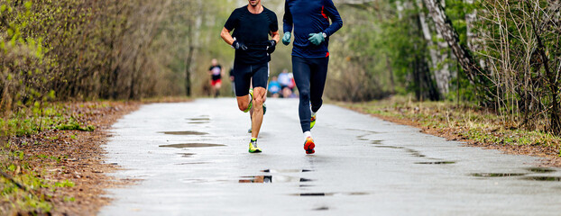 two male runners run race on wet road in forest