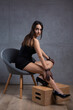 © Budjak Studio - Classic dark studio portrait of a young brunette woman in black clothes who is sitting on a chair against a concrete wall.
