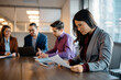 © Drazen - Asian businesswoman reads documents during meeting with coworkers in office.