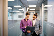 © Drazen - Happy businessmen using laptop while walking through hallway in office.