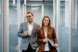 © Drazen - Happy businesswoman and her Hispanic male colleague in hallway looking at camera.