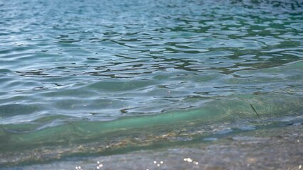 Wall Mural - Clear rather calm sea with small waves, sun reflects in water, some seaweed visible, closeup detail from the beach near