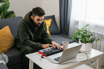 Wall Mural - Man music producer or arranger using laptop and midi keyboard and other audio equipment to create music at home studio. Beat making and arranging audio content and composing song concept