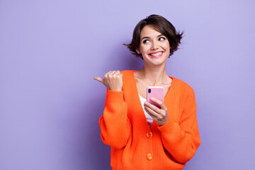 Photo of cute dreamy lady dressed orange cardigan texting modern device thumb empty space isolated purple color background